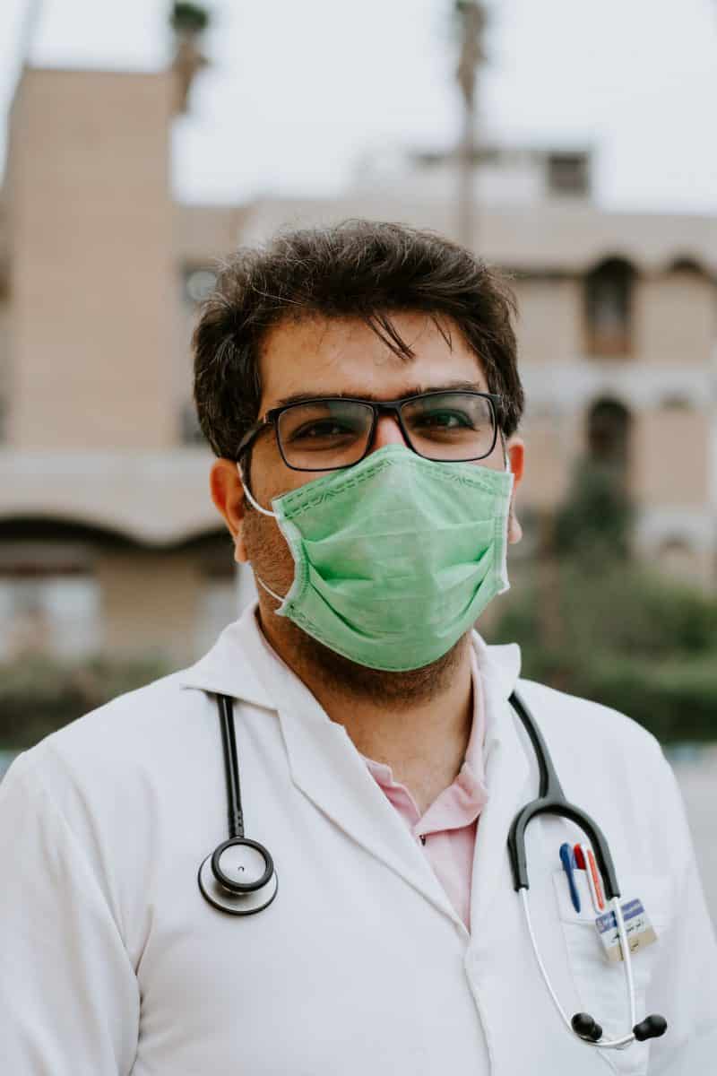 man in white scrub suit wearing green mask